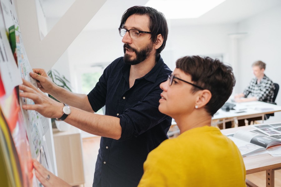Zwei Designer prüfen gemeinsam Entwürfe an einer Wand